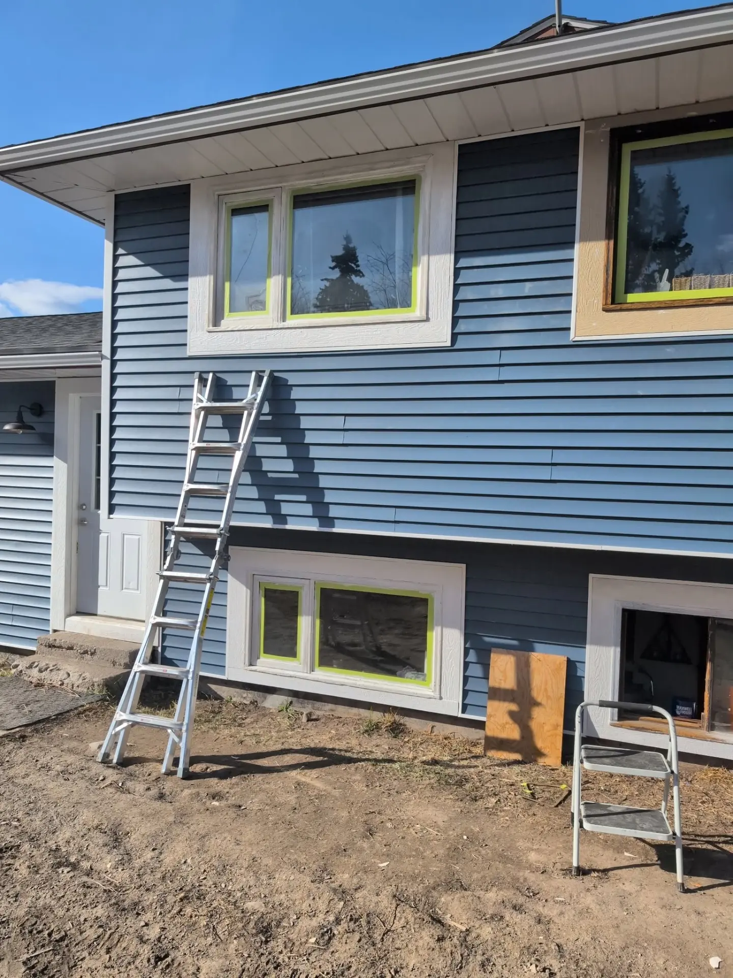 Blue-sided home with windows masked for trim and paint work